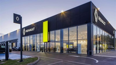 Zunanjost prodajnega salona Renault z osvetljenim razstavnim prostorom in parkiranimi vozili.