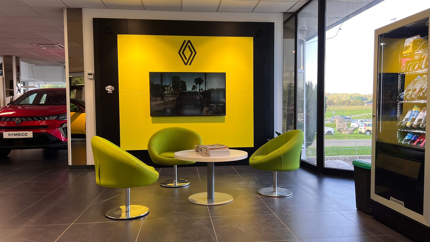 Notranjost poslovalnice Vrtin z rumeno steno, zaslonom in sedežno garnituro.