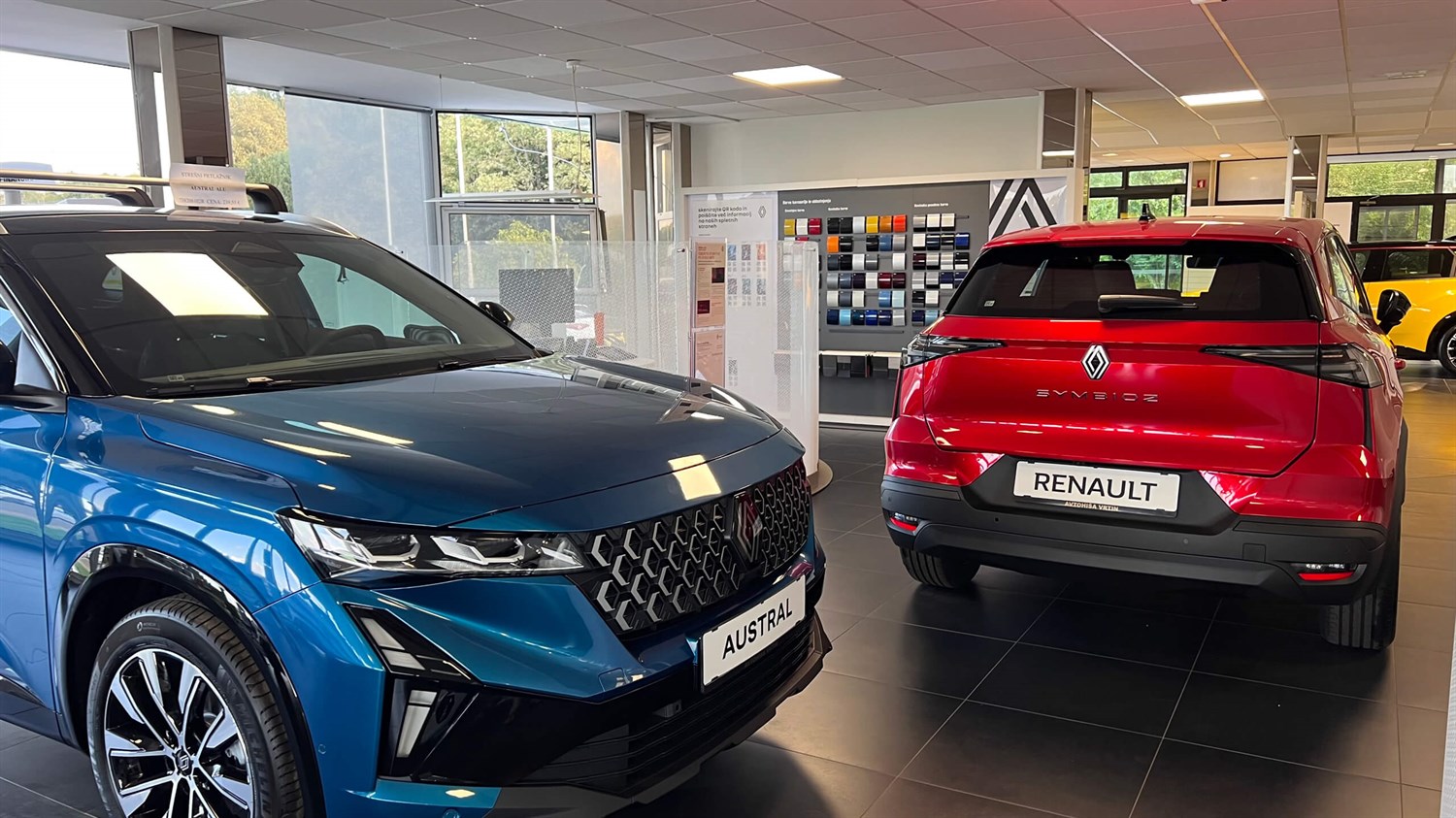 Dva Renault vozila, modri in rdeči, razstavljena v notranjosti poslovalnice Vrtin.