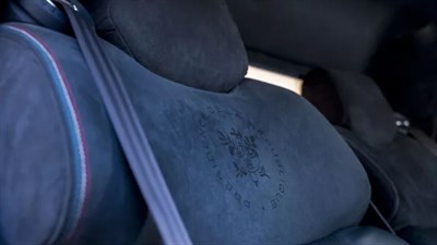 Bližnji posnetek modrega avtomobilskega sedeža z vtisnjenim emblemom in varnostnim pasom.
