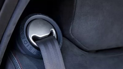 Bližnji posnetek modrega avtomobilskega sedeža z vtisnjenim emblemom in varnostnim pasom.