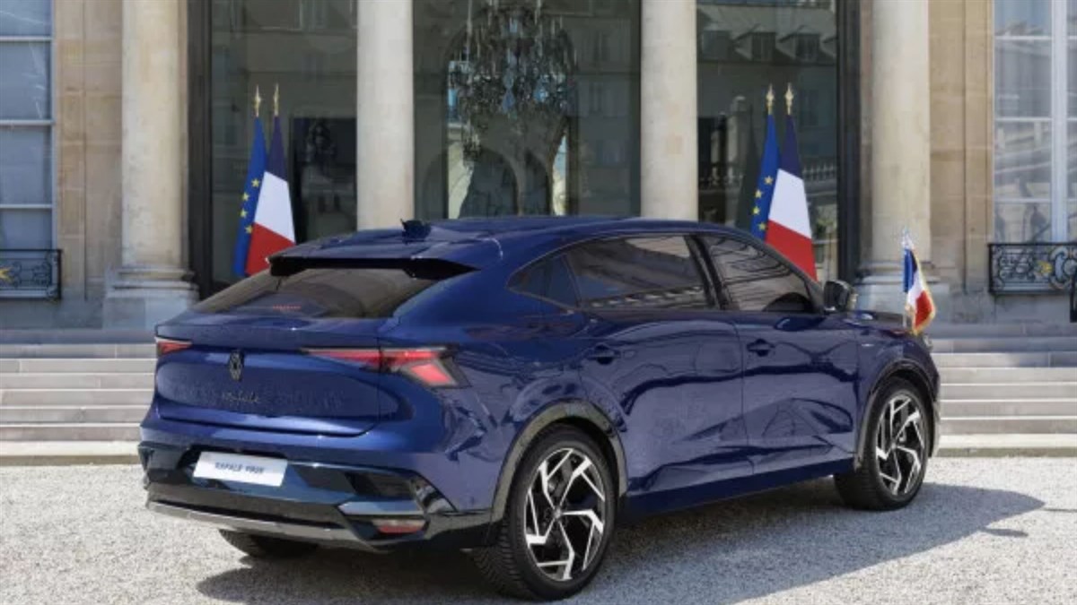 Temno moder Renault Rafale stoji na prodnatem dvorišču. Za njim je velika neoklasična fasada z visokimi okni in stebri; nad vhodom visijo francoske zastave, dve manjši stojita ob vozilu.
