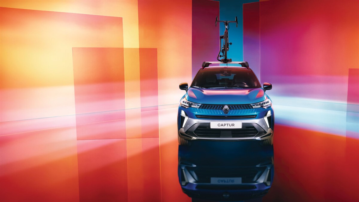 Na sliki je moder Renault Captur, prikazan od spredaj. Na strehi vozila je nameščeno kolo na prtljažniku.
