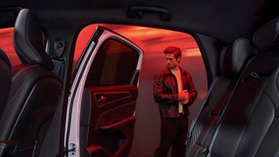 ChatGPT said:
Na sliki je pogled iz notranjosti vozila Renault, s poudarkom na zadnjih sedežih in odprtih zadnjih vratih. V ozadju, v rdeče osvetljenem prostoru, stoji moški v usnjeni jakni, ki ustvarja dinamičen in samozavesten vtis. 