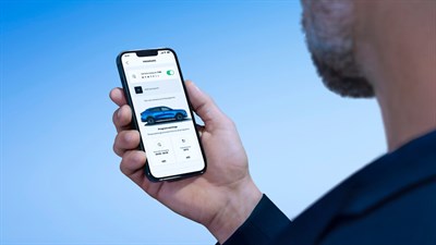 Na sliki je moški, ki v roki drži pametni telefon z odprto aplikacijo za upravljanje vozila Renault. Na zaslonu je prikazana možnost programiranja nastavitev, kot sta časovno načrtovano polnjenje vozila in nastavitev temperature v notranjosti. 