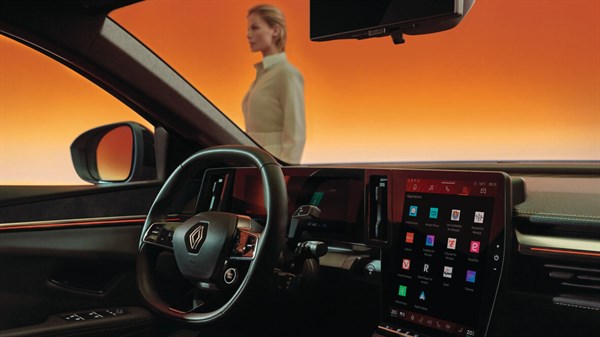 Ženska hodi pred parkiranim vozilom Renault oblečena v svetla elegantna oblačila.
