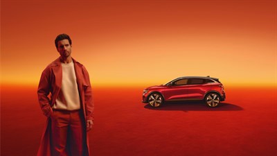 Moški stoji pred parkiranim rdečim Megane E-Tech vozilom.