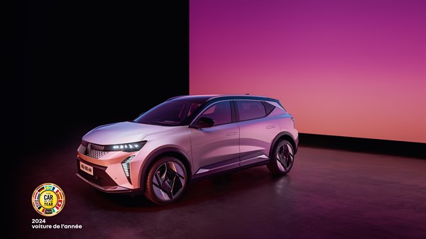 Beli Renault Scenic E-Tech parkiran v prostoru z vijolično-roza osvetlitvijo, spodaj znak za nagrado "Car of the Year 2024".