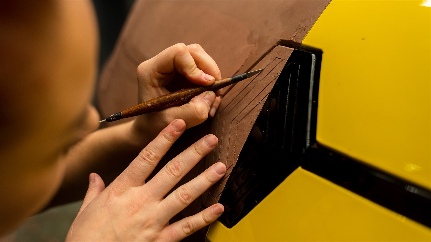 Oblikovalec ročno riše linije logotipa Renault na rumeni karoseriji vozila.