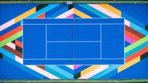 Barvito teniško igrišče z geometrijskim vzorcem okoli modre igralne površine.