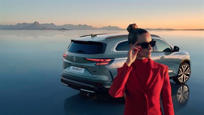 Renault Espace parkiran ob mirni vodni površini, v ospredju ženska v rdečem suknjiču.