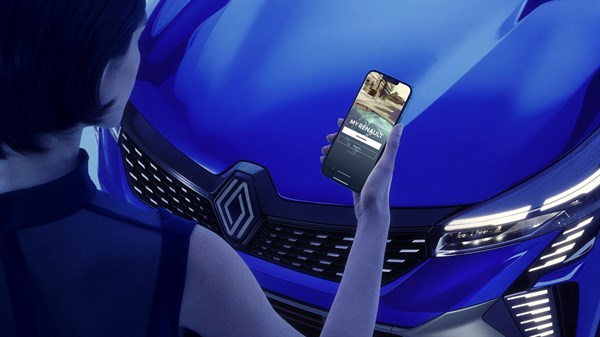 Ženska stoji pred modrim avtomobilom in drži pametni telefon z odprto aplikacijo My Renault.