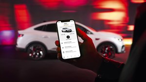 Oseba drži pametni telefon z aplikacijo My Renault pred belim vozilom Renault zamegljinm v ozadju.