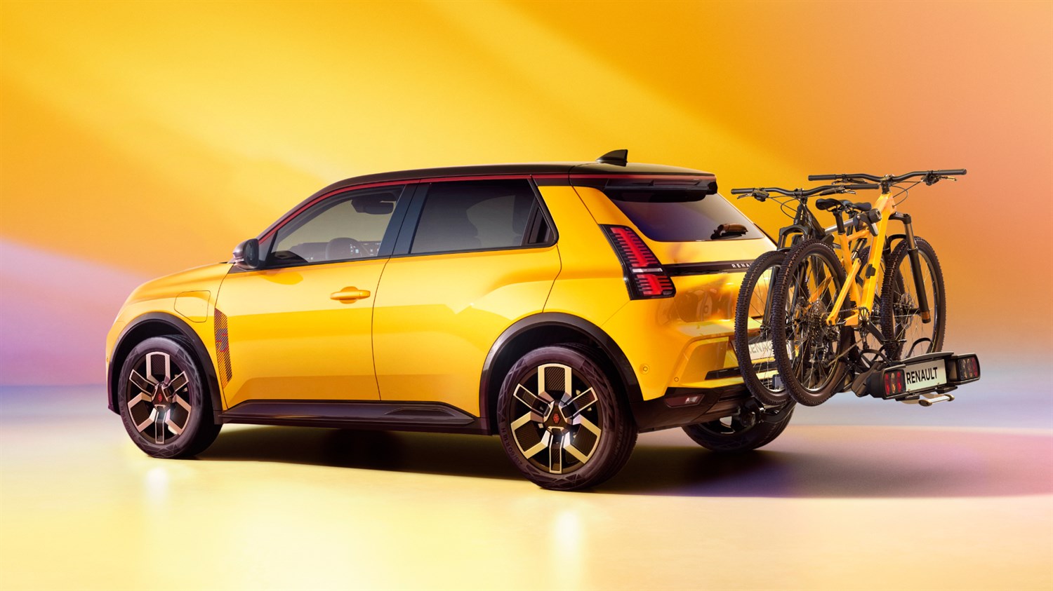 Renault 5 E-Tech rumene barve s pritrjenim nosilcem za kolesa na zadnjem delu.