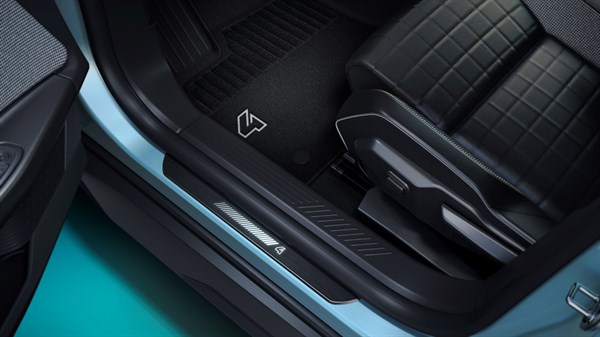 Prag na vstopnem delu kabine Renault 4 E-Tech Electric z osvetljenim logotipom in preprogo ob voznikovem sedežu.