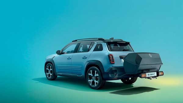 Modro-sivi Renault 4 E-Tech Electric v ¾ pogledu z desne zadnje strani, s priklopnim prtljažnim nosilcem in velikim, temno sivim kovčkom.