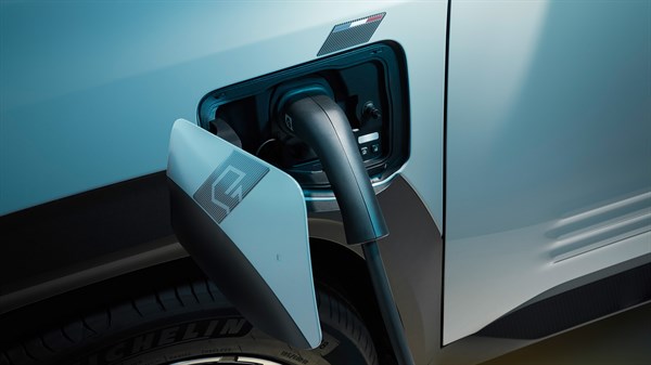 Odprt pokrov polnilnega vtiča na levi sprednji strani Renault 4 E-Tech Electric z vstavljenim polnilnim kablom.