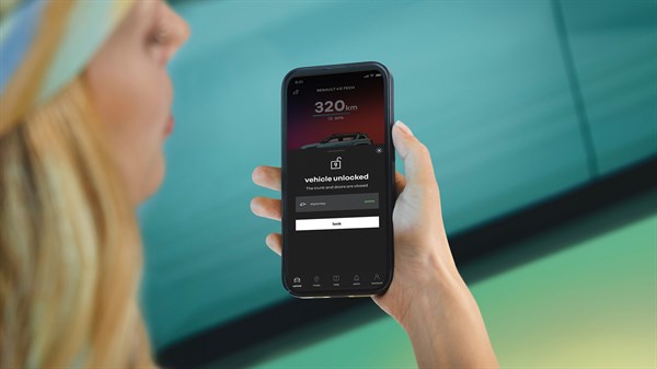 Svetlolasa ženska drži telefon z aplikacijo My Renault, na zaslonu prikazan doseg 320 km, stanje “vozilo odklenjeno” in gumb za zaklepanje.