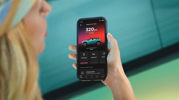 Svetlolasa ženska drži telefon z aplikacijo My Renault, na zaslonu prikazan doseg 320 km, sliko Renault 4 E-Tech Electric in ikone za klimatizacijo, ogrevanje ter druge funkcije.