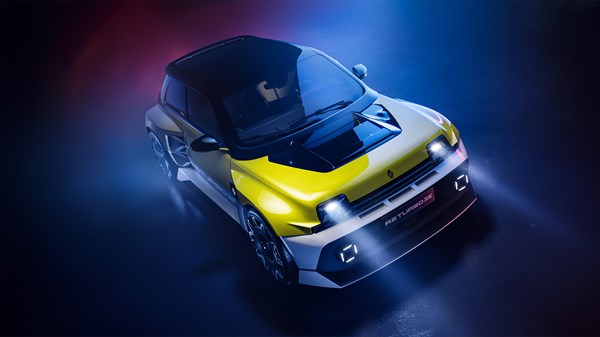 Zgornji pogled na Renault 5 Turbo 3E v rumeno-sivi barvi, s prižganimi žarometi v temnem prostoru z modro-rdečo osvetlitvijo.