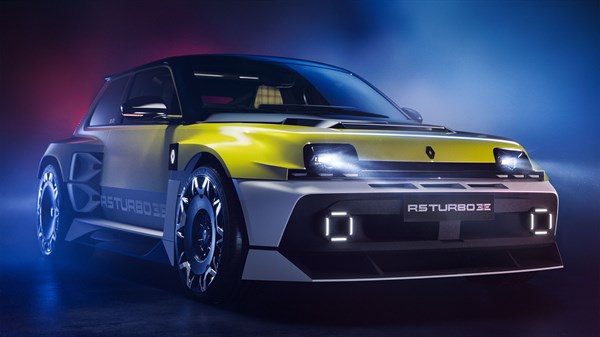 Stranski sprednji pogled na Renault 5 Turbo 3E, z rumeno-sivo karoserijo in prižganimi LED žarometi v temnem prostoru z modro-rdečo svetlobo.