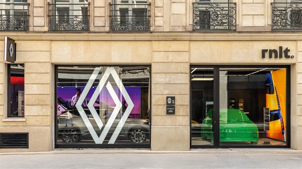Zunanjost razstavnega salona rnlt s stekleno fasado in velikim logotipom Renault, skozi okna je viden zelen avtomobil in barvna notranjost salona.