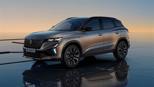 Sodoben SUV Renault Austral z dinamično obliko in LED žarometi, parkiran na odsevni površini ob sončnem zahodu.