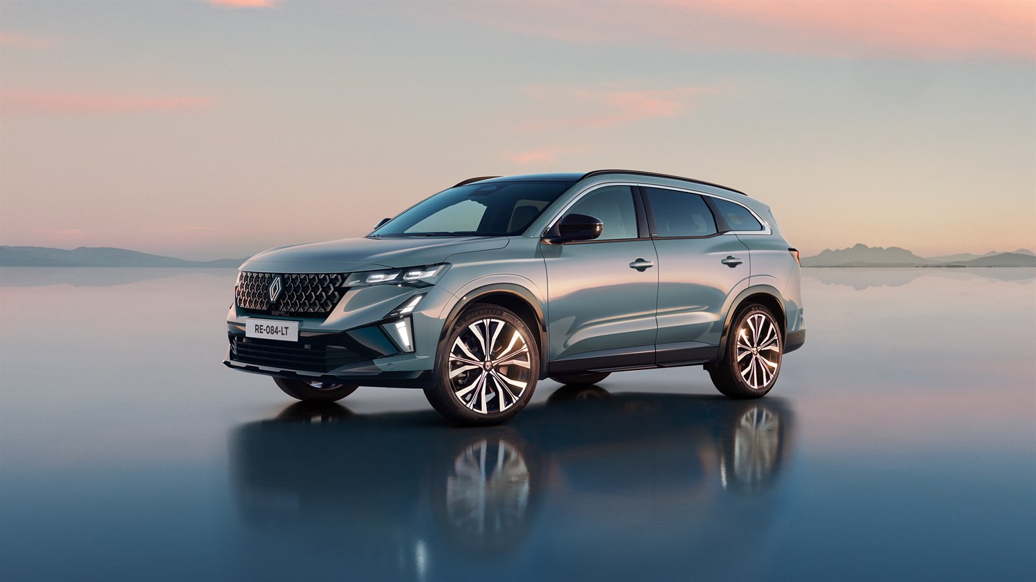 Renault Espace v svetlo modrozeleni barvi stoji na zrcalni površini ob sončnem zahodu, z odbojem vozila v tleh.
