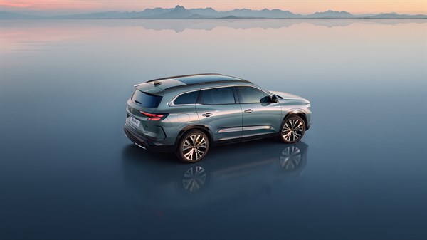 Ženska v svetlem kostimu hodi mimo parkiranega modrega Renaulta Espace.