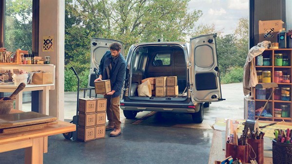 Renault Kangoo Van z odprtimi zadnjimi vrati pred skladiščem. Dva delavca nalagata tovor v prostoren tovorni del vozila.