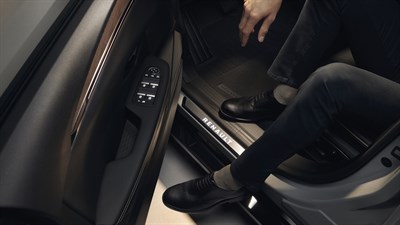 Moški stopa v vozilo Renault Megane E-Tech, pogled usmerjen na prag z osvetljenim napisom Renault in nadzorno ploščo na voznikovih vratih.