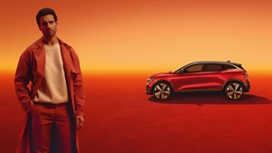Moški v modni opravi stoji ob vozilu Renault Megane E-Tech 100% Electric, ki je parkiran v studijskem ambientu z oranžno-rdečo osvetlitvijo.