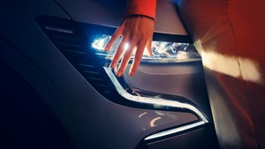 Roka se nežno dotika sprednjega LED žarometa vozila Renault Megane E-Tech 100% Electric, ki sveti v temi.