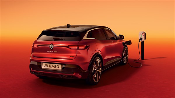 Renault Megane E-Tech priključen na polnilno postajo, posnet od zadaj pod kotom na oranžno-rdečem ozadju.
