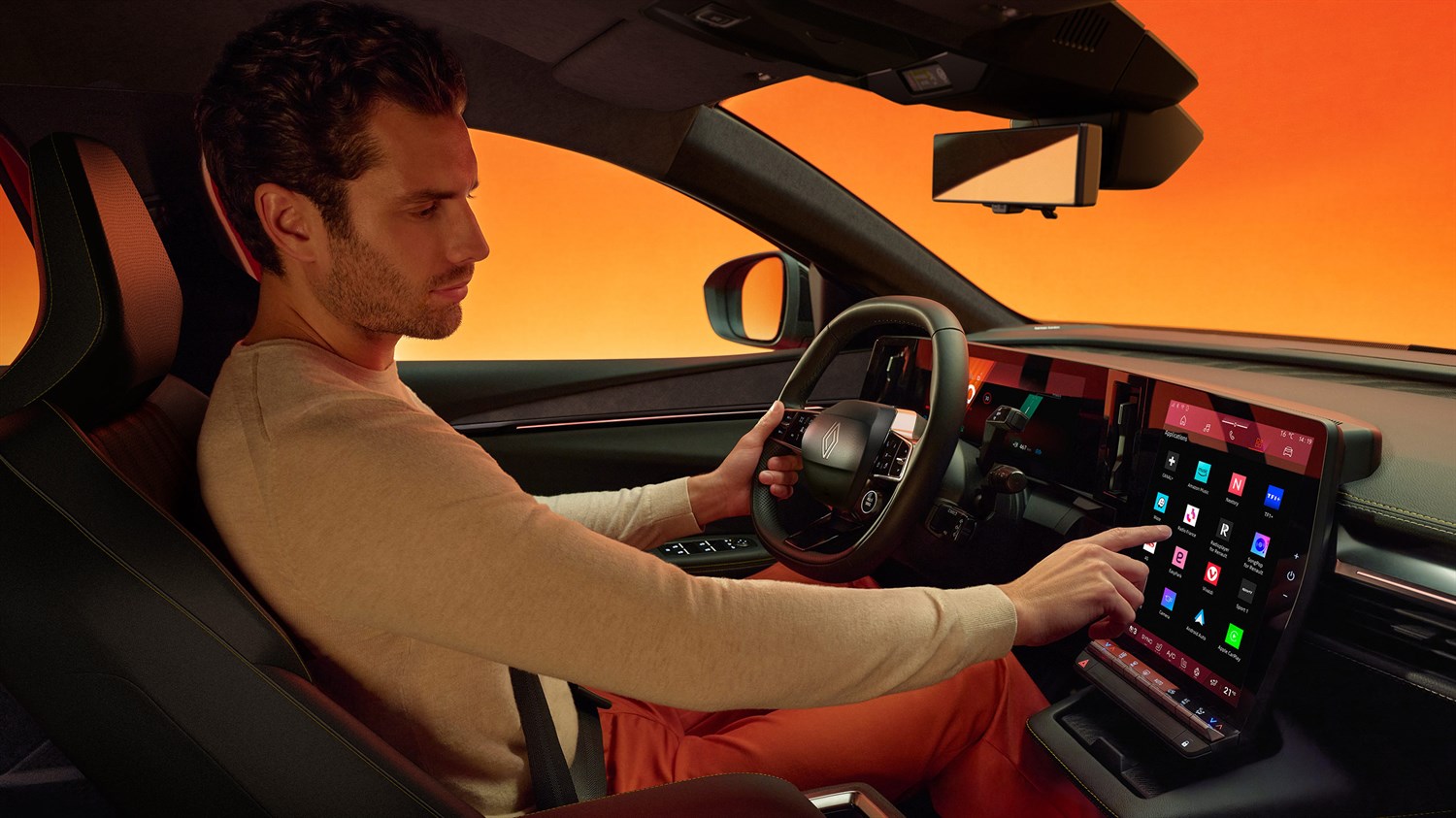 Moški na voznikovem sedežu Renault Megane E-Tech Electric upravlja velik osrednji zaslon na dotik, z ambientno osvetlitvijo in oranžno-rdečim ozadjem skozi okna.