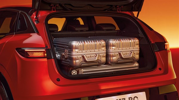Renault Megane E-Tech vozilo rdeče odprt prtljažnik s kovčki na oranžnem ozadju