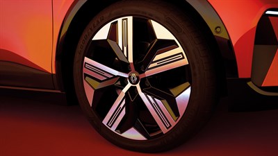 Podrobnost športnega aluminijastega platišča z logotipom Renault na vozilu Renault Megane E-Tech Electric, osvetljenega z večernimi odtenki oranžne svetlobe.