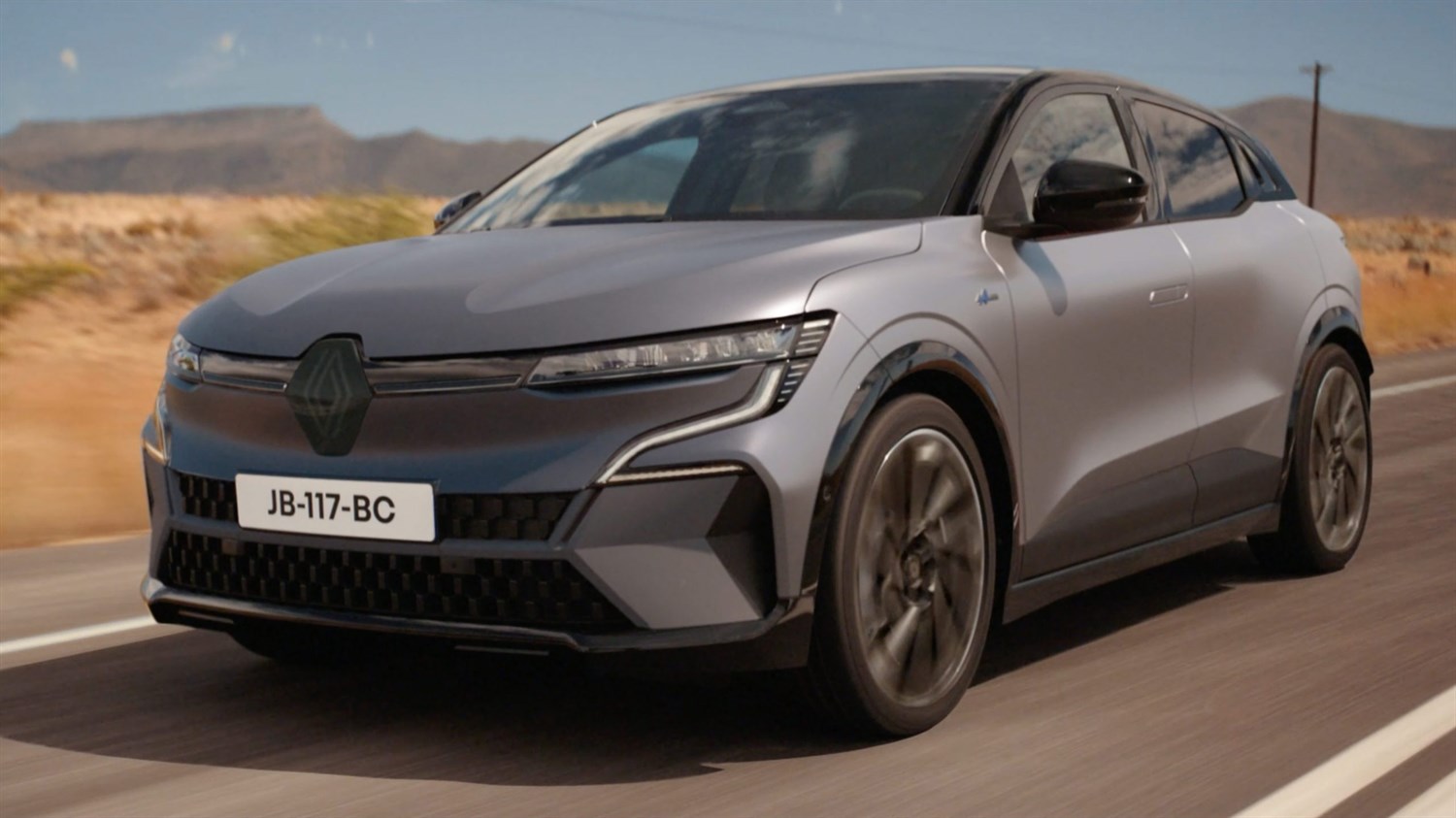 Siv Renault Megane E-Tech v vožnji po cesti v puščavskem okolju, posnet od spredaj pod kotom.