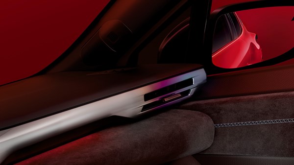 Notranjost rdečega Renault Clio; bližnji posnetek leve zračne reže, armaturne obloge in stranskega ogledala v rdeči osvetlitvi.