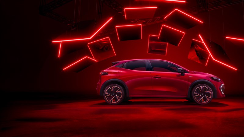 Rdeč Renault Clio v stranskem profilu v rdeče osvetljenem studiu, nad vozilom viseče neonske linije in paneli.