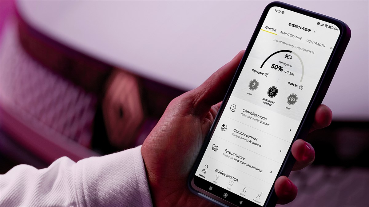 Oseba drži pametni telefon z odprto aplikacijo za Renault Scenic, prikaz stanja baterije in drugih informacij o vozilu. V ozadju je del sprednjega dela avtomobila.