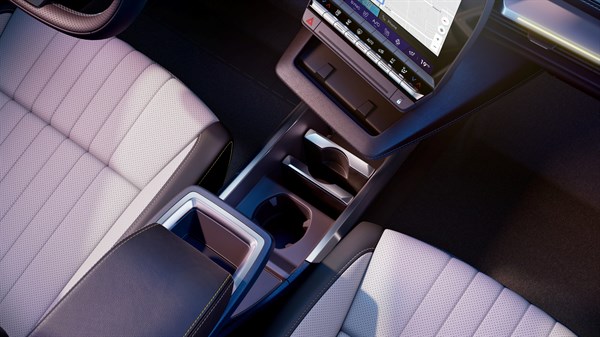 Pogled od zgoraj na sprednjo sredinsko konzolo, ki vključuje držala za pijačo, prostor za shranjevanje in roko naslon z oblazinjenim pokrovom med voznikovim in sovoznikovim sedežem.