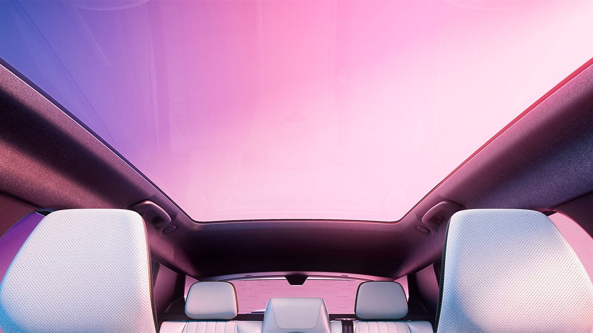 Pogled iz notranjosti Renault Scenic proti veliki panoramski stekleni strehi z rožnato-vijolično svetlobo.