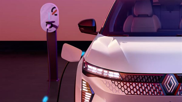 Renault Scenic E-Tech med polnjenjem na polnilnici, prikazan spredaj z leve strani v vijolični osvetlitvi.