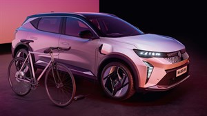 Na sliki je sodoben bel električni SUV Renault, parkiran v osvetljenem studiu z rožnato-vijolično svetlobo.