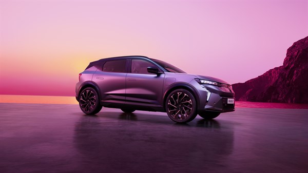 Renault Scenic E-Tech electric v temno vijolični barvi parkiran ob obali ob sončnem zahodu z rožnatim nebom in skalnato obalo v ozadju.