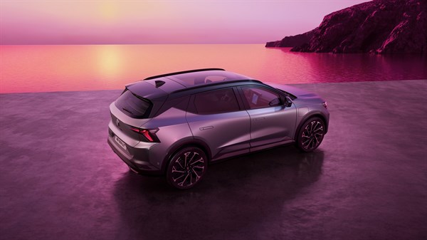 Renault Scenic E-Tech electric v srebrni barvi, pogled od zgoraj zadaj, parkiran ob mirnem morju ob sončnem zahodu z rožnatim nebom in skalnato obalo v ozadju.