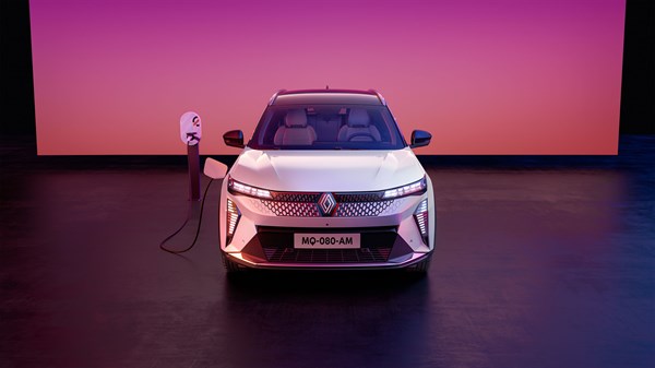 Renault Scenic E-Tech electric v srebrni barvi, pogled od spredaj, priključen na polnilnico na odprti površini ob rožnatem sončnem zahodu.