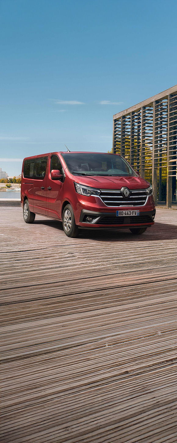 Renault Trafic Passenger v elegantni rdeči barvi, parkiran ob vodi v urbanem okolju – sodoben in prostoren kombi za prevoz več potnikov.