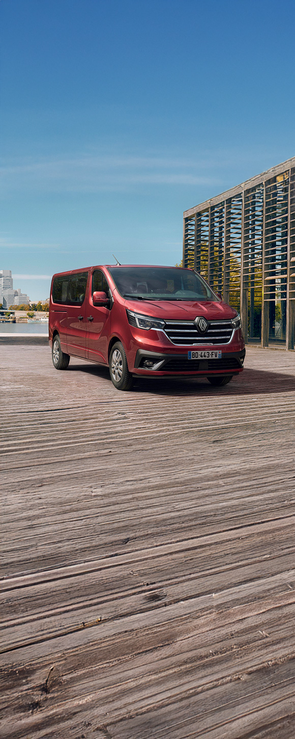 Renault Trafic Passenger v elegantni rdeči barvi, parkiran ob vodi v urbanem okolju – sodoben in prostoren kombi za prevoz več potnikov.